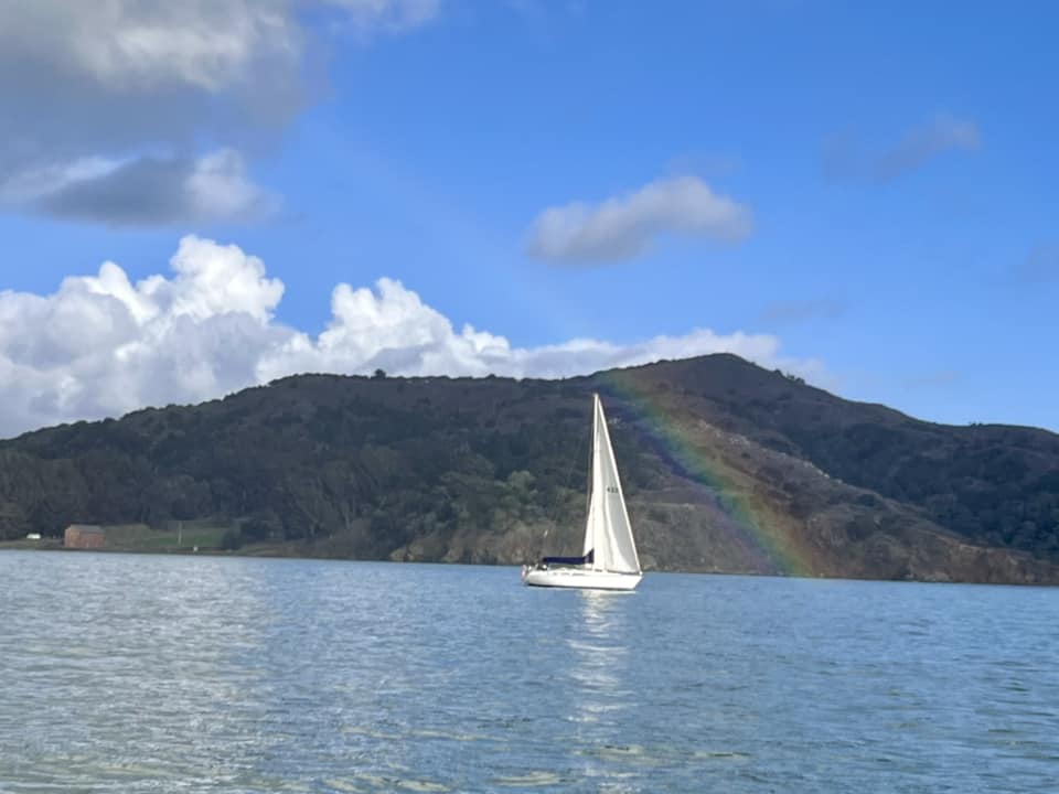 Sailboat sailing in front of mountains with a rainbow over it.